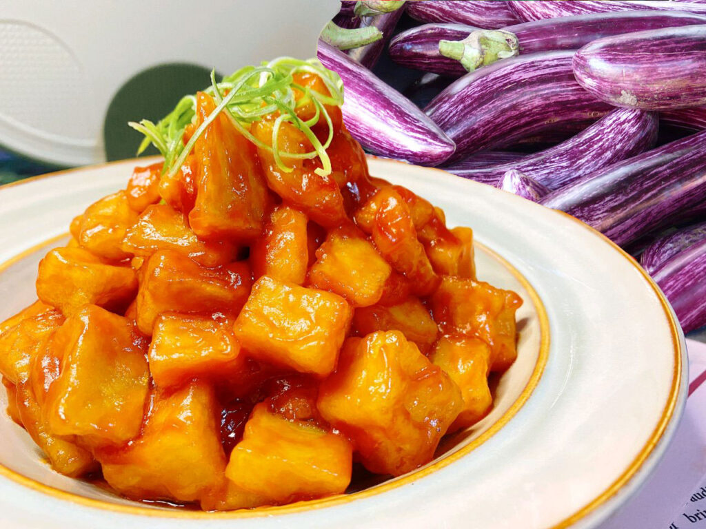 sweet and sour eggplant in a plate，with a lot of eggplants behind