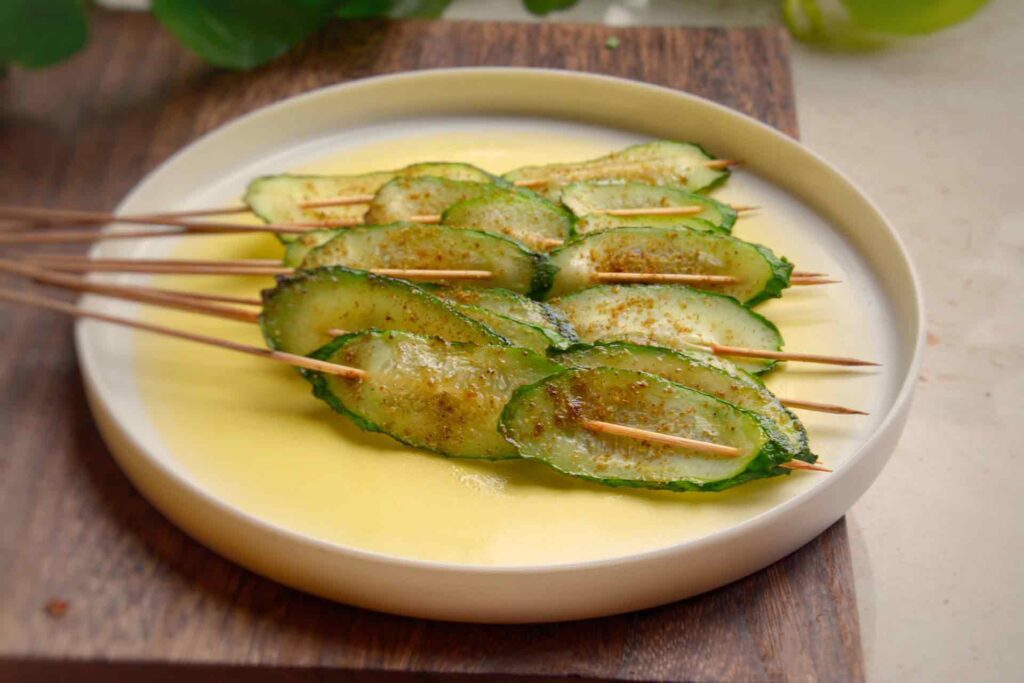  Roasted Cucumber, cucumber slices are threaded  onto skewers,on a white plate