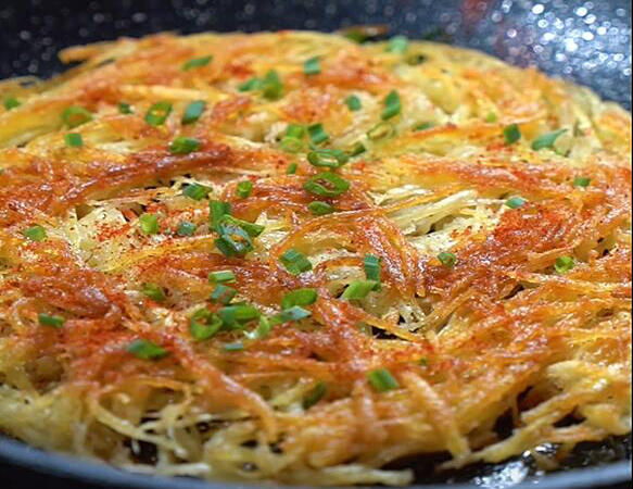 yellow brown Shredded potato pancake in a black plate with some chopped green onions