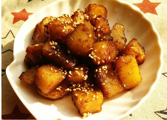 Sweet and sour potato pieces in a shell shape plate with some sesame seeds 