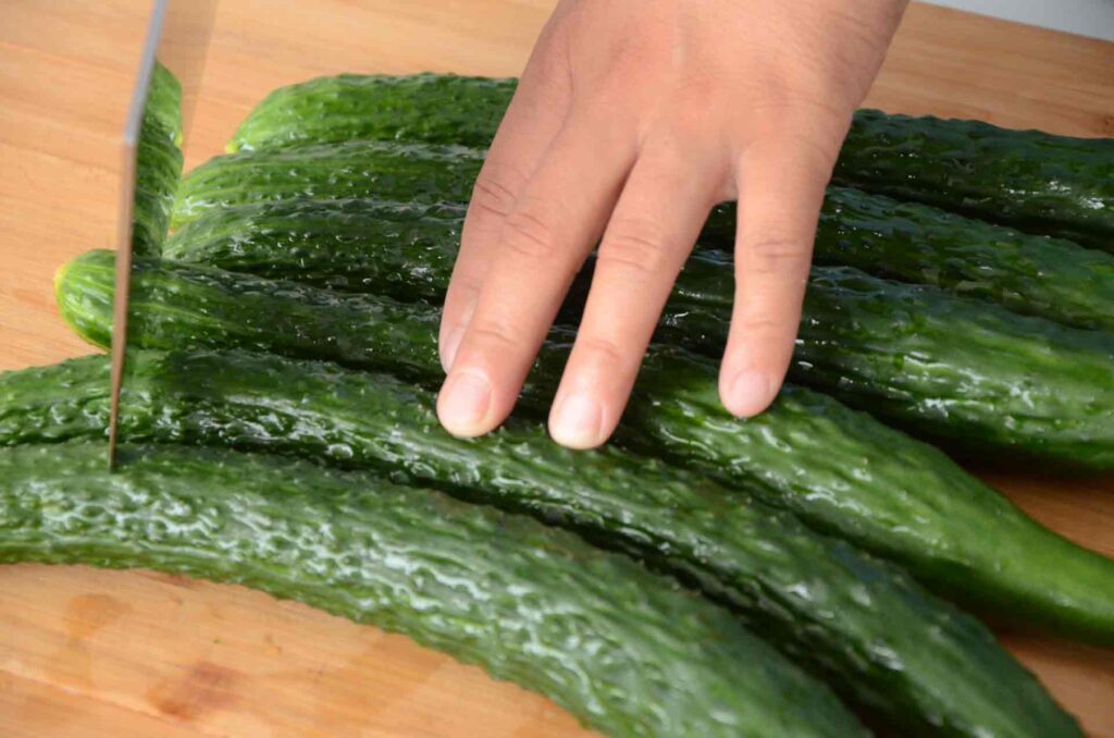 one hand press some cucumbers and a knife cut cucumbers