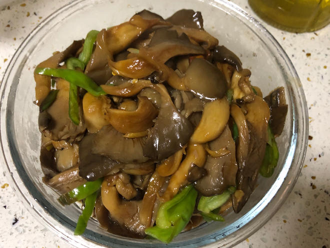 brown stir-fry oyster mushroom with some green pepper in a glass bowl